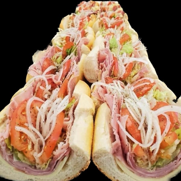 Several deli subs from Ana's Corner Store, filled with meats, cheese, tomatoes, lettuce, and onions.