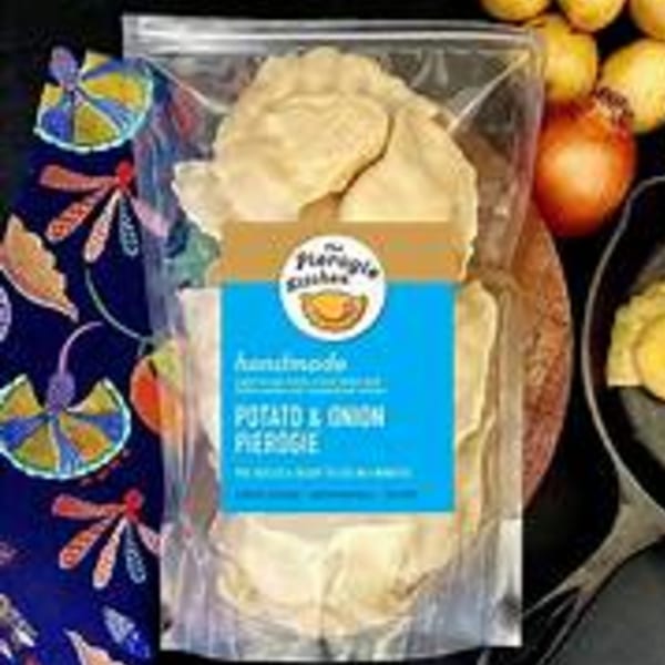 A bag of Ana's Corner Store potato and onion pierogies, with onions and a colorful cloth.