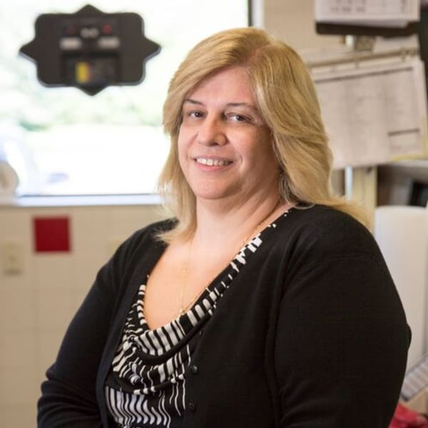 A smiling blonde woman wearing a black cardigan and striped top stands in Ana's Corner Store.