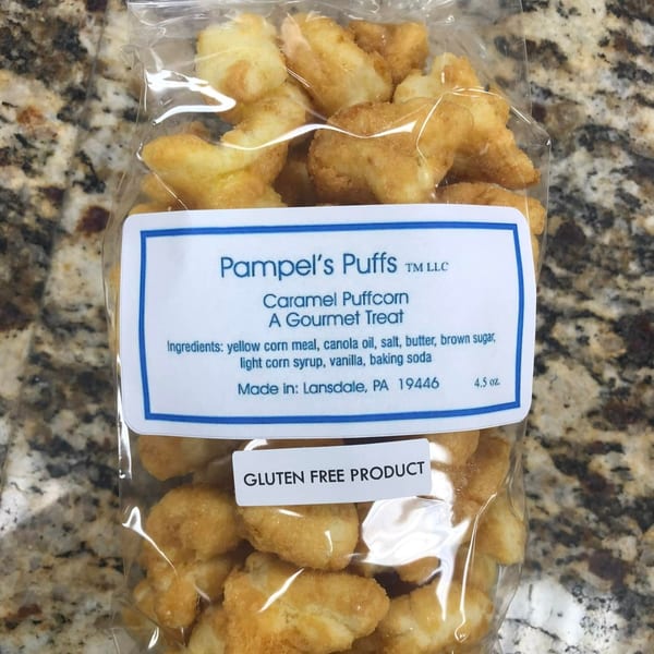 A clear bag of Pampel's Puffs Caramel Puffcorn, a gluten-free gourmet treat, on a speckled counter.