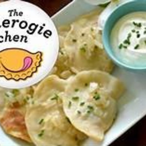Plate of pierogi with a side of sour cream and chives, with a logo overlay.