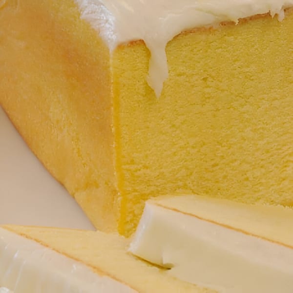 Close-up of a yellow pound cake loaf with white icing dripping down, and a slice cut off.