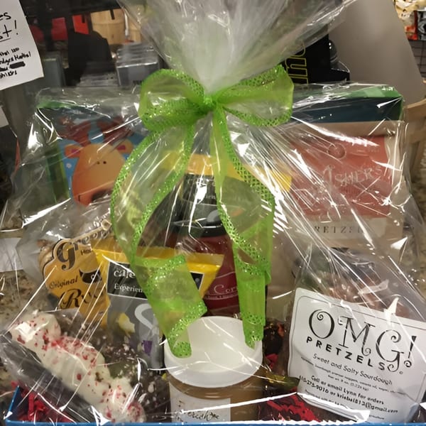 A deli gift basket filled with snacks, coffee, and pretzels, wrapped in cellophane with a green bow.