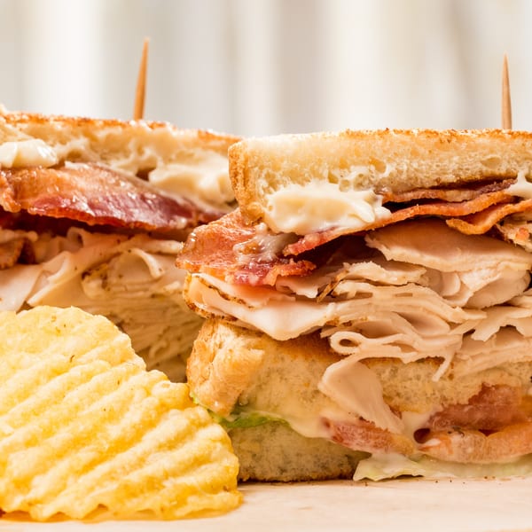 Two halves of a deli club sandwich with turkey, bacon, and mayonnaise, served with chips.