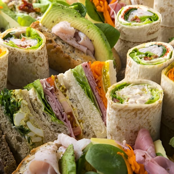 A deli platter with various sandwiches, wraps, and avocado-topped bread, showcasing fresh ingredients.