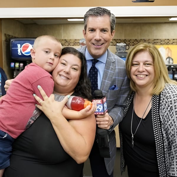 A TV reporter with a microphone poses with two women and a child in Ana's Corner Store.