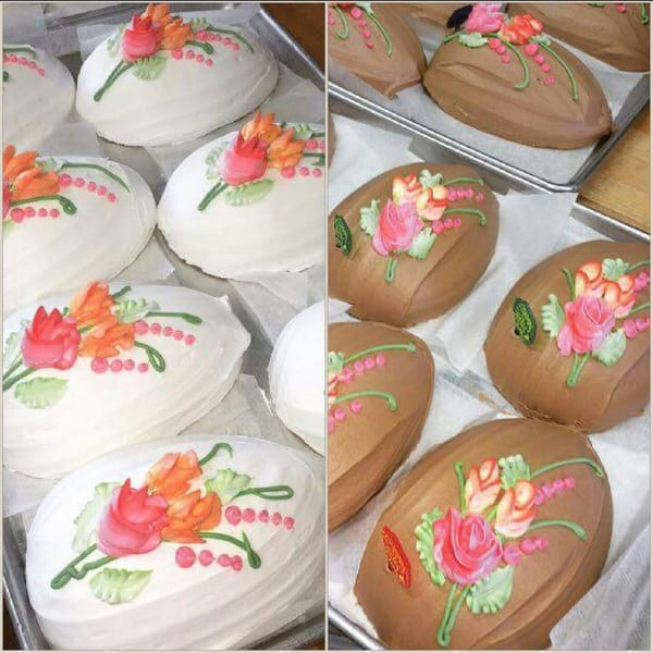 White and brown oval cakes with pink, orange, and green floral icing designs on baking sheets.