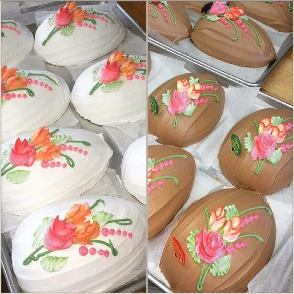 White and brown oval cakes with pink, orange, and green floral icing designs on baking sheets.
