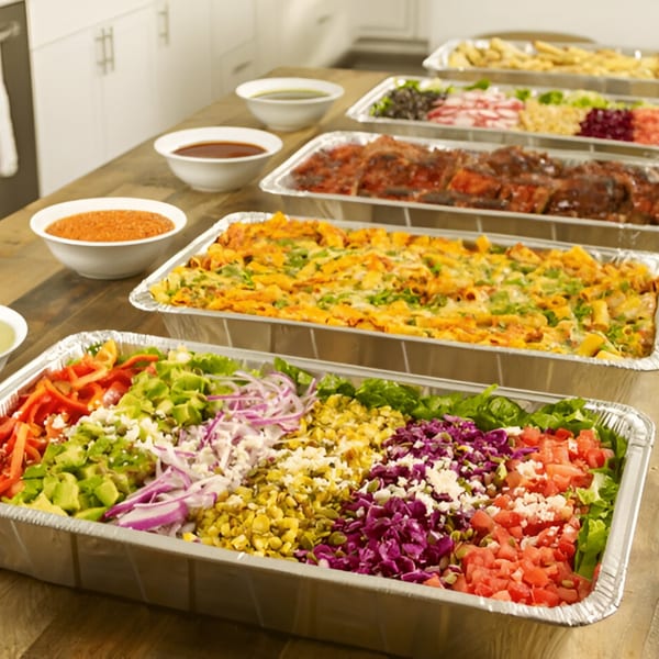 Ana's Corner Store deli catering spread with salads, pasta, and ribs in aluminum trays.