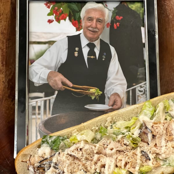 A deli sandwich with chicken, lettuce, and dressing, in front of a framed photo of a man.