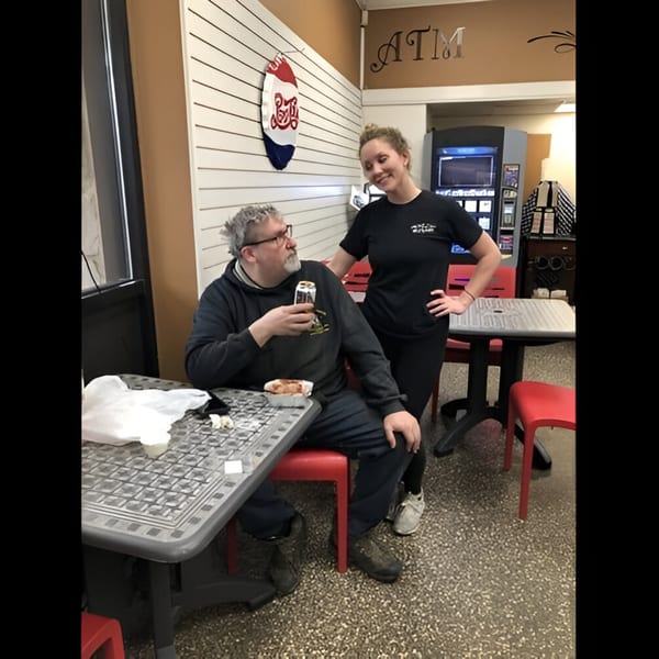 A man with a drink and a woman smiling in a deli with an ATM and Pepsi sign.