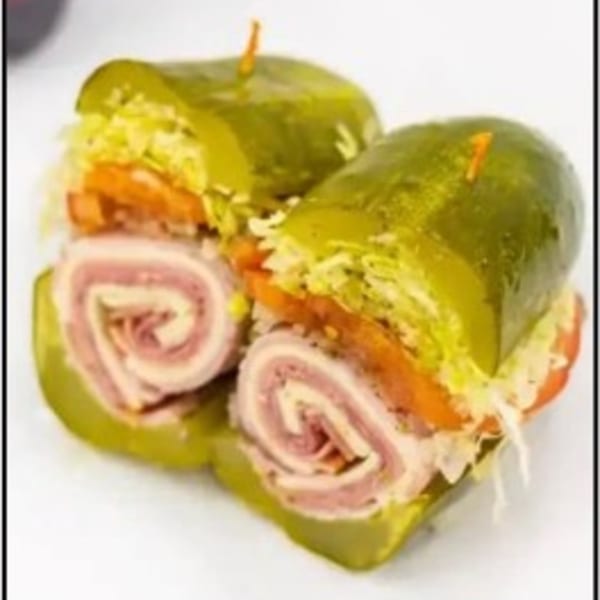Two deli pickle sandwiches, cut in half, filled with rolled meats, cheese, lettuce, and tomato.