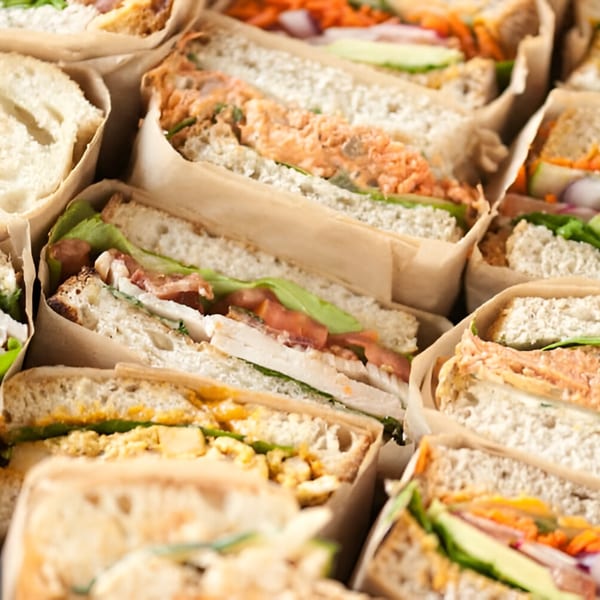 Assortment of deli sandwiches from Ana's Corner Store, wrapped in paper, showcasing various fillings.