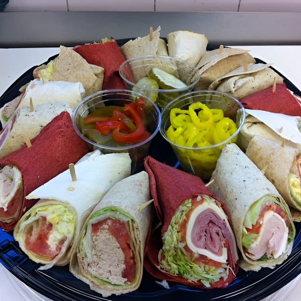 A deli platter with various wraps, including red and white tortillas, alongside cups of pickles and peppers.