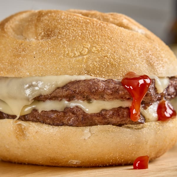 Close-up of a double cheeseburger with melted cheese and ketchup dripping down the side.
