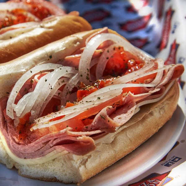 Close-up of a deli sub sandwich with meat, cheese, tomatoes, and onions on a white plate.