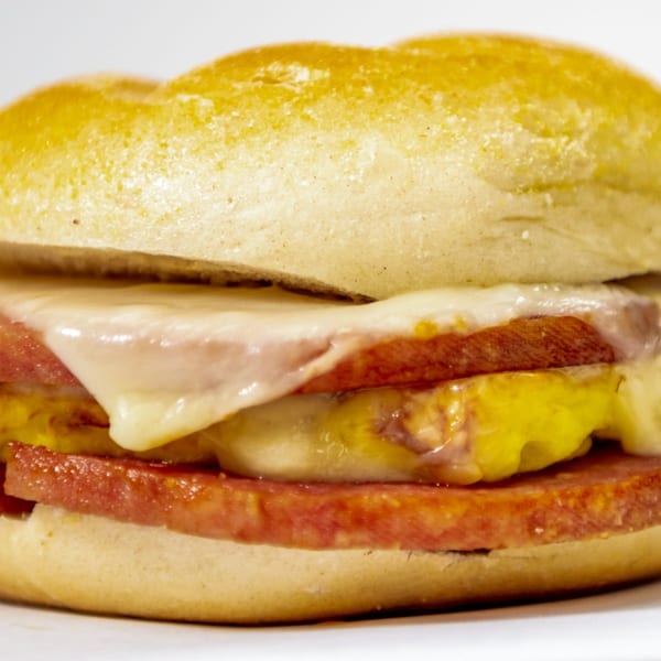 Close-up of a deli sandwich with melted cheese, yellow mustard, and thick-cut meat on a bun.